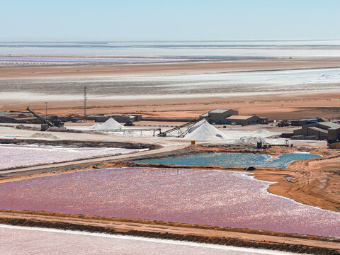 Aerial view of industrial salt production facilities, pink evaporation ponds, and white salt piles in the desert landscape of Walvis Bay, Namibia.