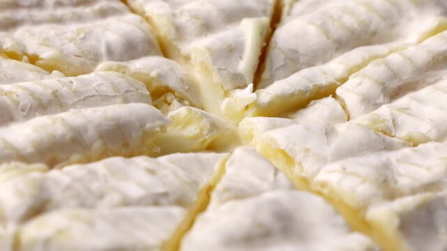 Creamy brie or camembert cheese wheel cut into wedges, soft white rind revealing gooey paleyellow interior circle rotation close up