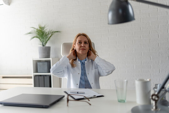 Doctor stretching her neck after long hours at work. Neck pain, muscle tension, poor posture, workplace ergonomics and occupational health awareness concept