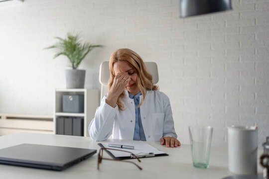 Overwhelmed doctor reviewing paperwork at her desk. Administrative burden, healthcare documentation, physician stress, medical records and clinical workload concept