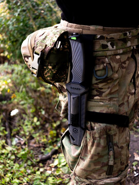 Tactical fixed blade knife in black sheath attached to a thigh rig of a person wearing camouflage uniform and outdoor survival gear, Ukrainian military.