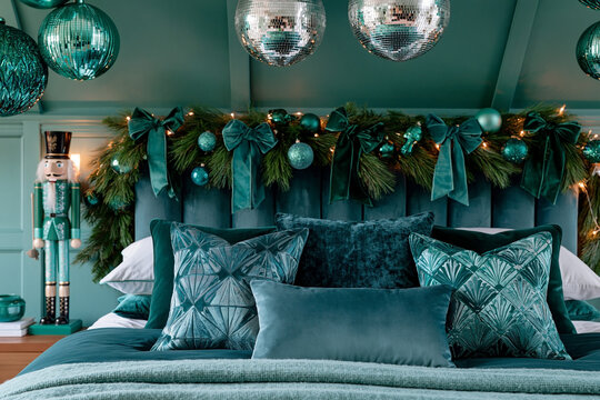 Luxurious teal bedroom interior featuring a plush bed adorned with decorative pillows, a festive garland, and shimmering ornaments hanging from the ceiling