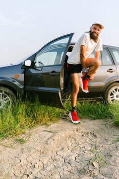 Man Puts on Shoes Next to His Car on a Dirt Road in Nature