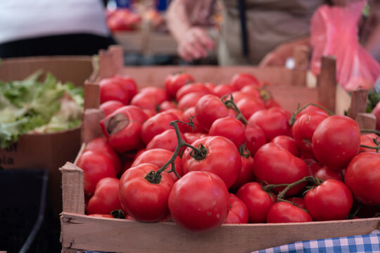 Ripe red farm-grown tomatoes in a wooden crate at a local farmers market, fresh seasonal produce and natural food concept