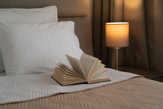 Open book resting on a bed in a cozy beige and brown bedroom, hotel, peaceful reading, relaxation and slow living concept
