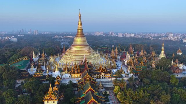 Aerial drone view at Shwedagon Pagoda, a golden stupa, surrounded by lush greenery and urban development in Yangon (Rangun), Myanmar (Burma), showcasing the city's blend of religious and modern life.