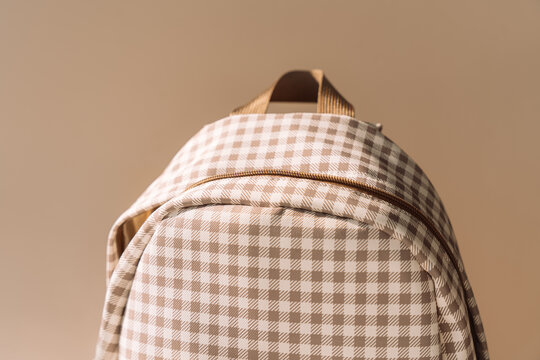 Beige checkered school backpack in warm sunlight, minimal back to school background.