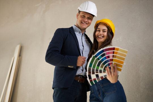 Smiling couple holding color swatches and looking at camera at construction site.