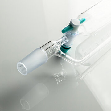 Glass separatory funnel with stopcock valve and ground joint on reflective background; Detail of laboratory addition funnel stopcock and ground glass cone joint.