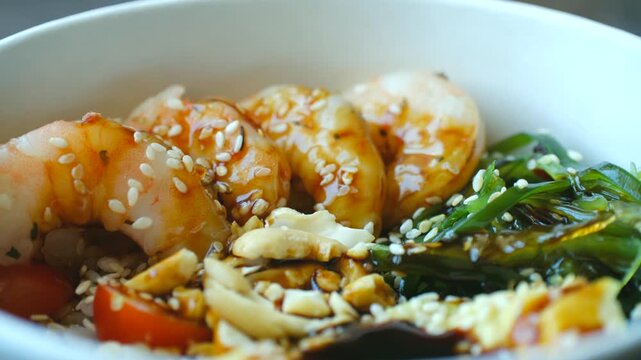 Freshly prepared poke bowl with grilled shrimp, wakame seaweed, peanuts, and cherry tomatoes over a bed of rice. Healthy and traditional asian cuisine meal concept for a nutritious lunch