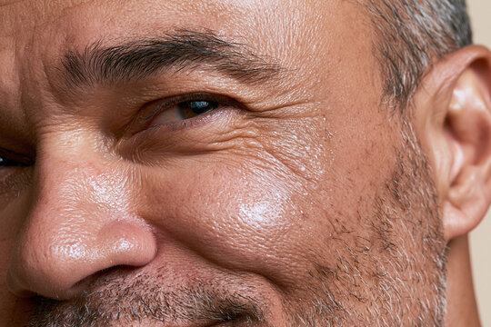 Close up macro portrait of mature man skin with visible wrinkles pores and stubble showing healthy moisturized complexion and gentle smile