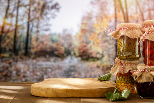 Homemade preserves in glass jars on wooden table with autumn landscape background.
