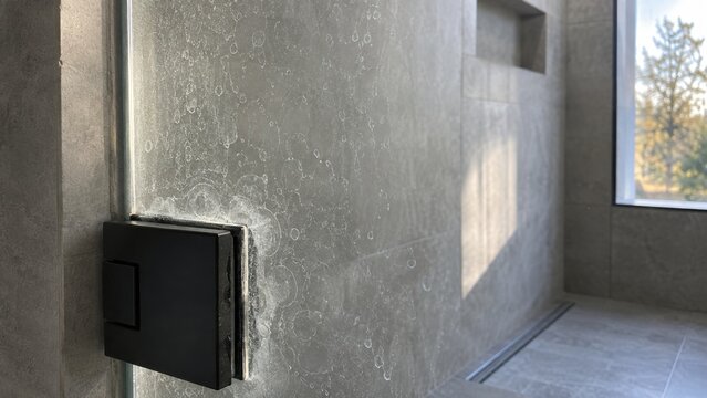 Matte black glass clamp on shower panel with limescale stains