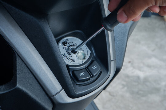 thief using a screwdriver tool to break into a motorcycle ignition lock, representing vehicle theft and security vulnerabilities. Ideal for news crime prevention campaigns, insurance agency websites