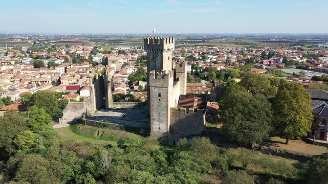 Aerial view of the historic Visconti Bridge and medieval castle ruins surrounded by lush trees and the town of Borghetto, Veneto, Italy.