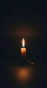 Single lit candle burning in deep darkness with warm golden glow darkness meditation