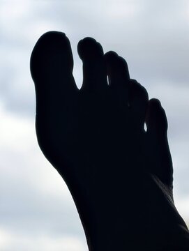 A dark shadow of a foot pointed up at a cloudy sky