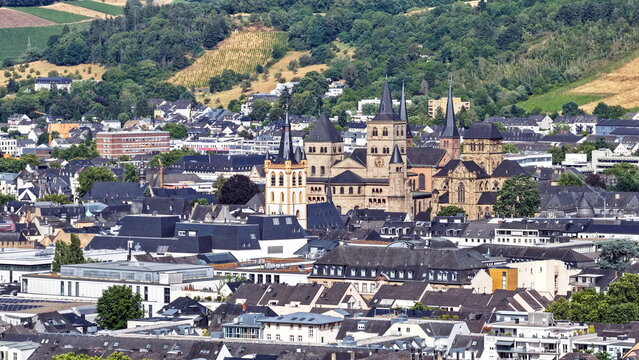 Malerische Stadtansicht von Trier mit dem monumentalen Dom und der Liebfrauenkirche inmitten von Wohnh&auml;usern vor den bewaldeten H&uuml;geln und Weinbergen des Moseltals.