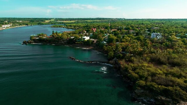Aerial view of the Boca Chavon river mouth meeting the Caribbean Sea, surrounded by lush tropical vegetation and coastal buildings in La Romana, La Romana, Dominican Republic.