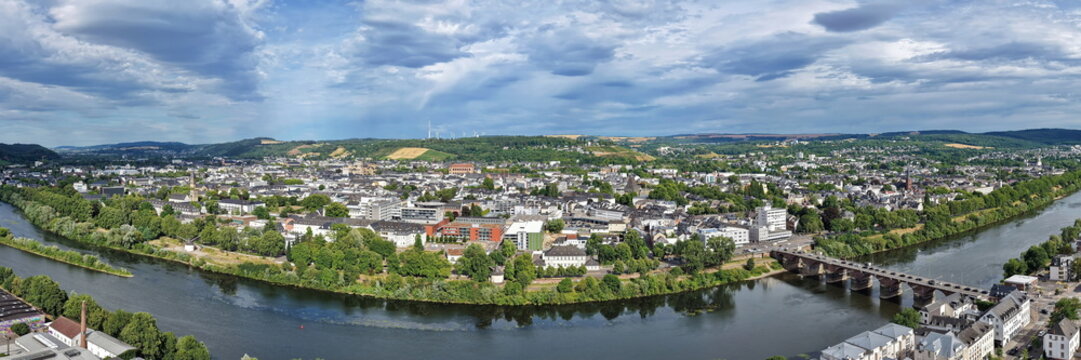 Luftbild von Trier mit der antiken R&ouml;merbr&uuml;cke &uuml;ber die Mosel, umgeben von Stadtarchitektur und gr&uuml;nen H&uuml;geln unter bew&ouml;lktem Himmel an einem Sommertag.