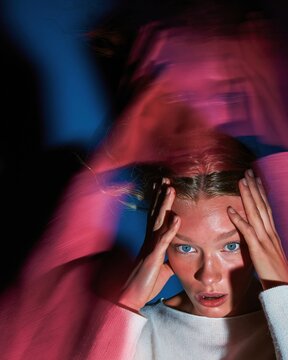 Stressed young woman with a startled expression holding her head in her hands, featuring motion blur for a mental health and anxiety concept
