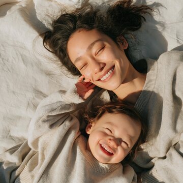 Tender mother and toddler lying on bed smiling in warm sunlight for family lifestyle wallpaper and cozy motherhood background