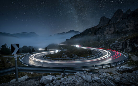 Long exposure photograph of car light trails on a winding mountain road at night, showcasing dynamic movement.