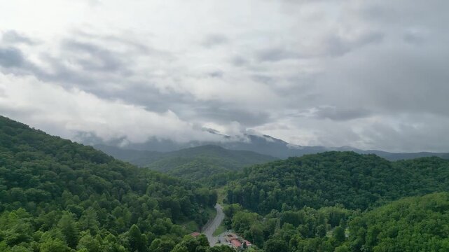 Aerial view near Cherokee, North Carolina, showing roads and buildings surrounded by lush forested mountains, low clouds, and drifting mist.