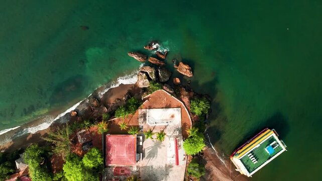 Aerial view of Boca Chavon featuring a coastal building, lush palm trees, rocky shoreline, and a boat in the turquoise waters of La Romana, La Romana, Dominican Republic.