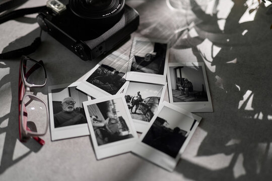 Old polaroid photos are placed around a camera and glasses on a table in a home setting