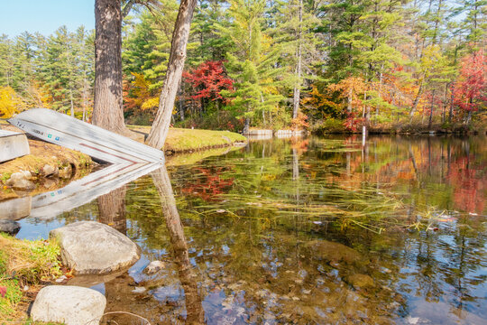 Peaceful Loon Lake swimming lake surrounded by multi-colored fall foliage in autumn, with a stack of colorful canoes piled on the coastline by water reflecting the imagery of the trees and blue sky