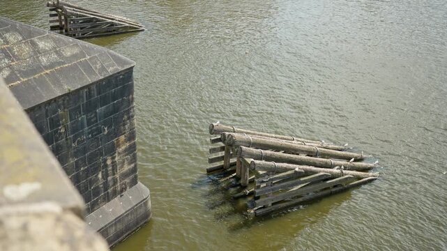 Heavy wooden icebreakers protect a stone pier of Charles Bridge on the Vltava River in Prague city. Traditional timber structures shield historic bridge pillars against floating river debris.