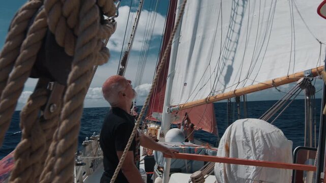 Old captain controls the crew working with the sails on the big expeditional sailing vessel moving in the Atlantic Ocean