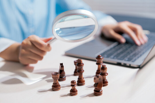 Business strategy concept. Magnifying glass examining chess pieces for competitive planning; analysis, leadership, risk, tactics, success