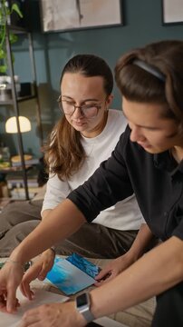 Vertical video of young diverse couple sitting on bed, selecting printed photographs and arranging them in photo album. Footage is suitable for family history and memory keeping campaigns
