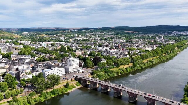 Luftbild von Trier mit der antiken R&ouml;merbr&uuml;cke &uuml;ber die Mosel, umgeben von Stadtarchitektur und gr&uuml;nen H&uuml;geln unter bew&ouml;lktem Himmel an einem Sommertag.