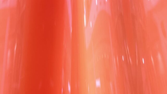 Translucent orange silicone slowly streams across a glossy folded surface