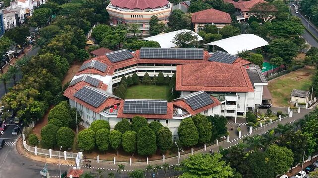 Aerial view of a circular building complex with solar panels on the roof surrounded by lush green trees and roads in Kecamatan Serpong, Banten, Indonesia.