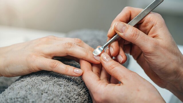 Close-up of a manicurist using a metal cuticle pusher on a client's fingernail