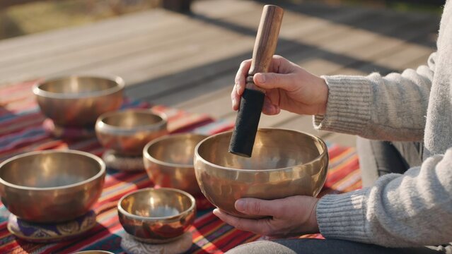 Person playing metal singing bowl with wooden mallet on striped fabric