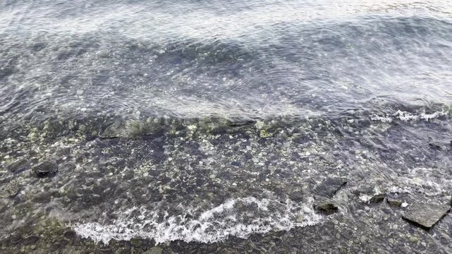 Gentle waves washing over a pebble beach on Lake Como, Italy