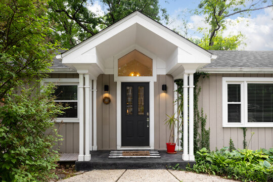 A black front door detail with glass windows under a tall white awning supported by white posts, brown vertical siding, and white trim. 