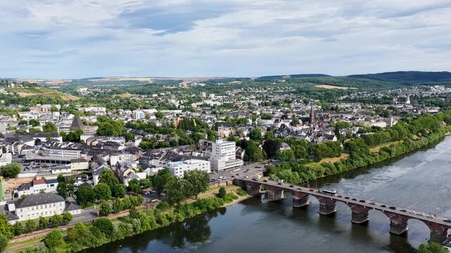 Luftbild von Trier mit der antiken R&ouml;merbr&uuml;cke &uuml;ber die Mosel, umgeben von Stadtarchitektur und gr&uuml;nen H&uuml;geln unter bew&ouml;lktem Himmel an einem Sommertag.