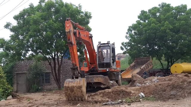 Orange heavy excavator working at construction site with dumper truck and industrial equipment
