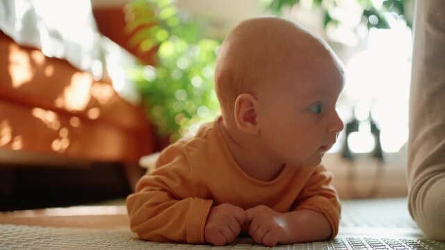Young baby with blue eyes lying on stomach during tummy time, learning to hold head up and strengthen neck muscles. Cute infant developing motor skills in a sunlit room with parental support