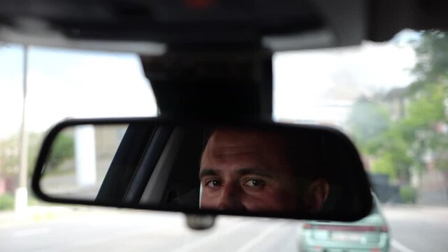 Eyes of male driver reflecting in rearview mirror while riding motor auto. Young man looking concentrated to urban road during operating electric vehicle. Confident guy driving modern car at city