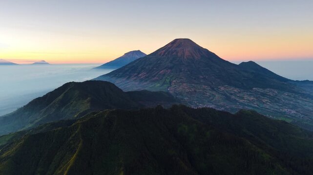 Aerial view of the volcanic Dieng Plateau landscape featuring towering mountain peaks, lush green slopes, and morning mist in Indonesia.