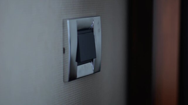 Male finger pressing light switch to turn off illumination in modern hotel room or home interior. Close up of hand controlling electricity and indoor lighting, showing energy saving concept