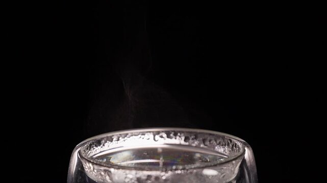 Steam Rises From Clear Glass of Hot Water Against Black Background, Showing Warmth and Refreshment