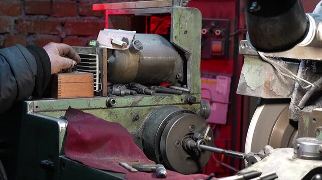Male hand of worker control precision metal threading process on industrial grinding machine in workshop. Rotating steel rod and abrasive wheel while manufacturing operation show machining technology.